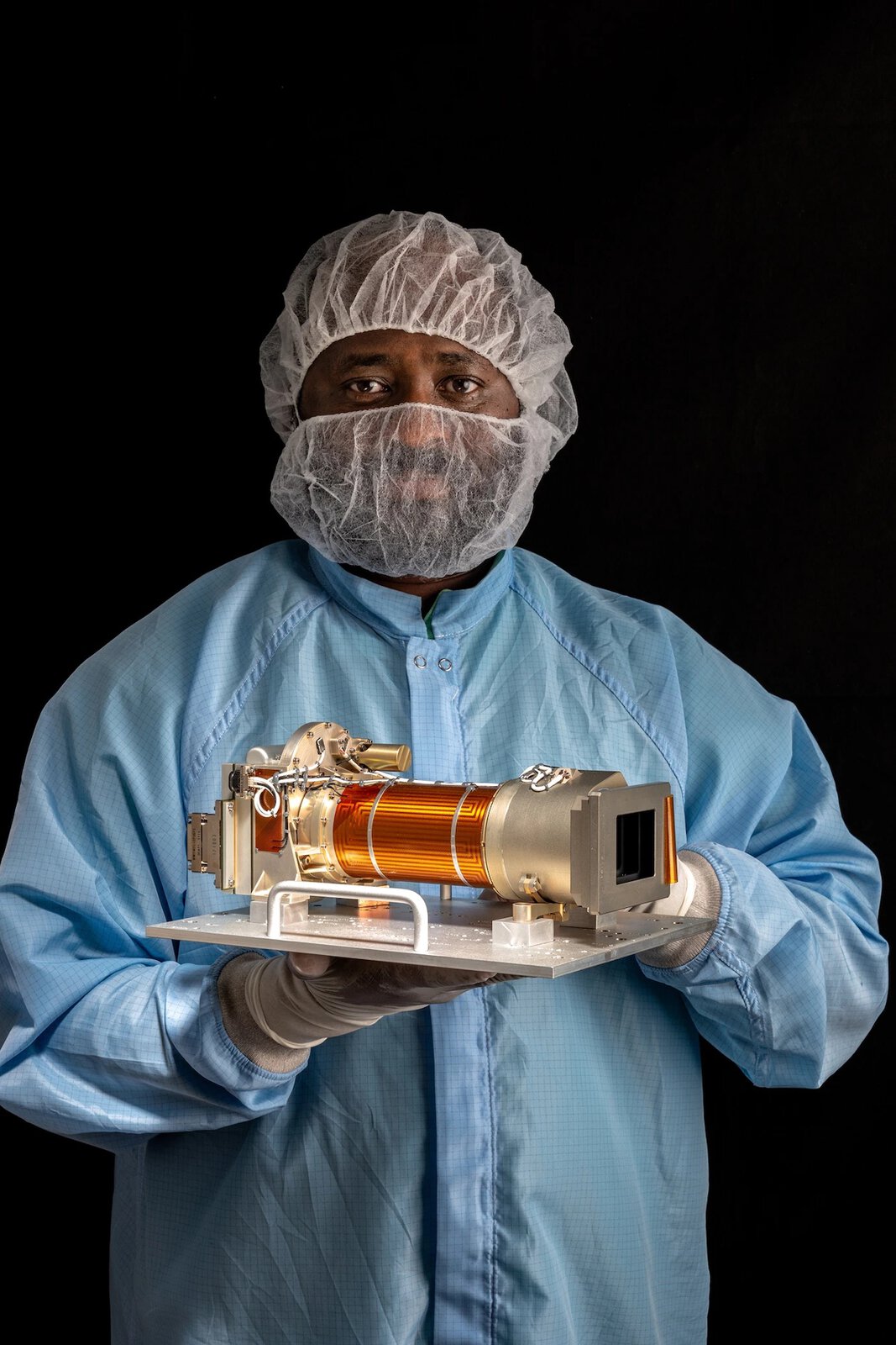 Kỹ thuật viên lắp ráp máy bay Olawale Oluwo của Hệ thống Khoa học Không gian Malin ở San Diego, California, đang cầm một bộ phận của Mastcam-Z, bộ đôi camera có khả năng thu phóng được lắp đặt trên tàu thăm dò Perseverance của NASA.