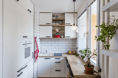 Khu vực bếp chữ I nhỏ gọn, màu trắng sáng, tích hợp tủ lạnh và lò vi sóng âm tủ, đối diện là bàn ăn gập treo tường